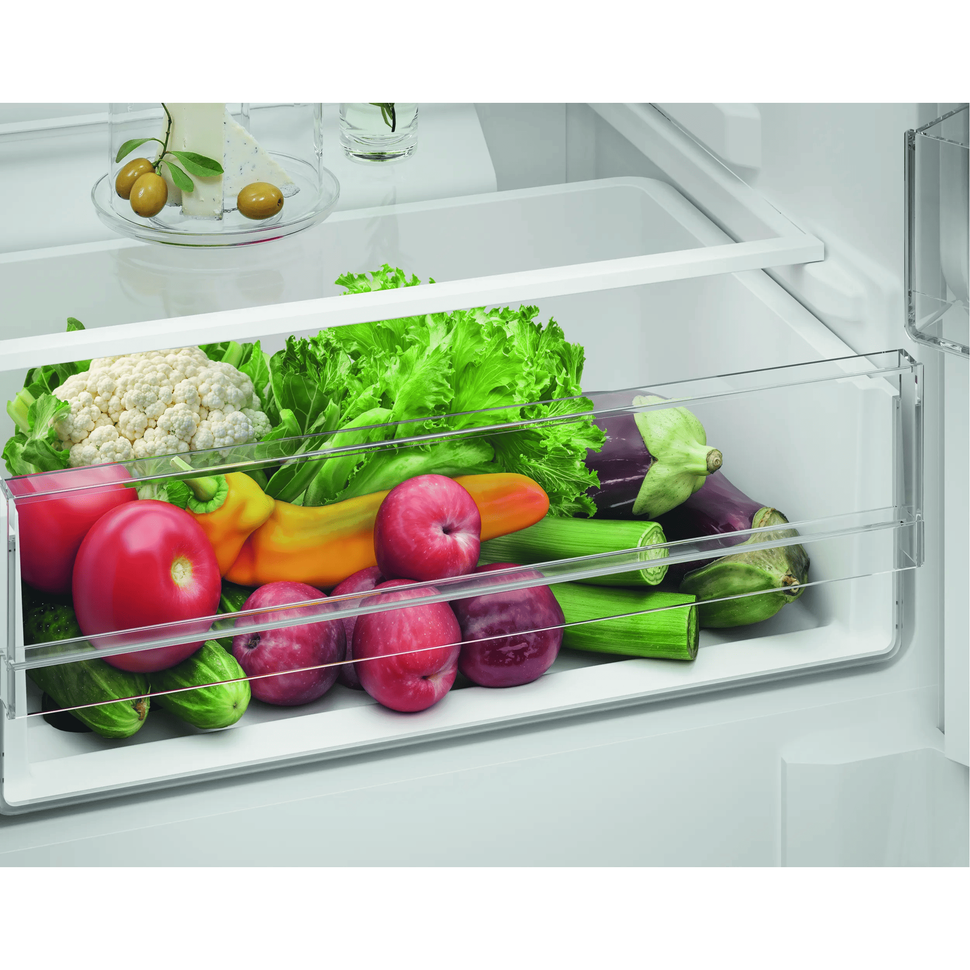Productos frescos en un cajón de verduras del refrigerador: lechuga, coliflor, tomates, pimientos, manzanas.
