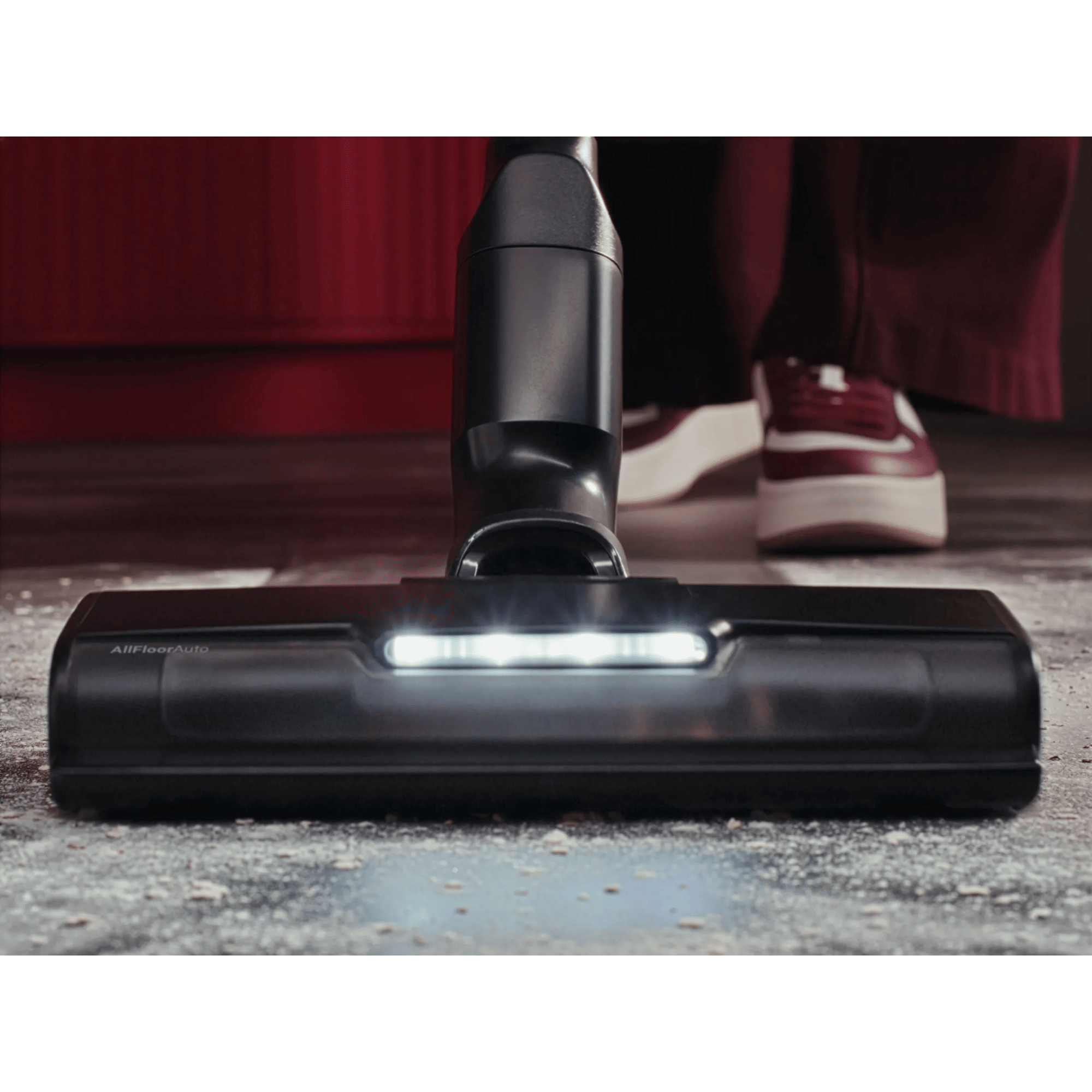 A black vacuum cleaner head with lights on a dirty floor.
