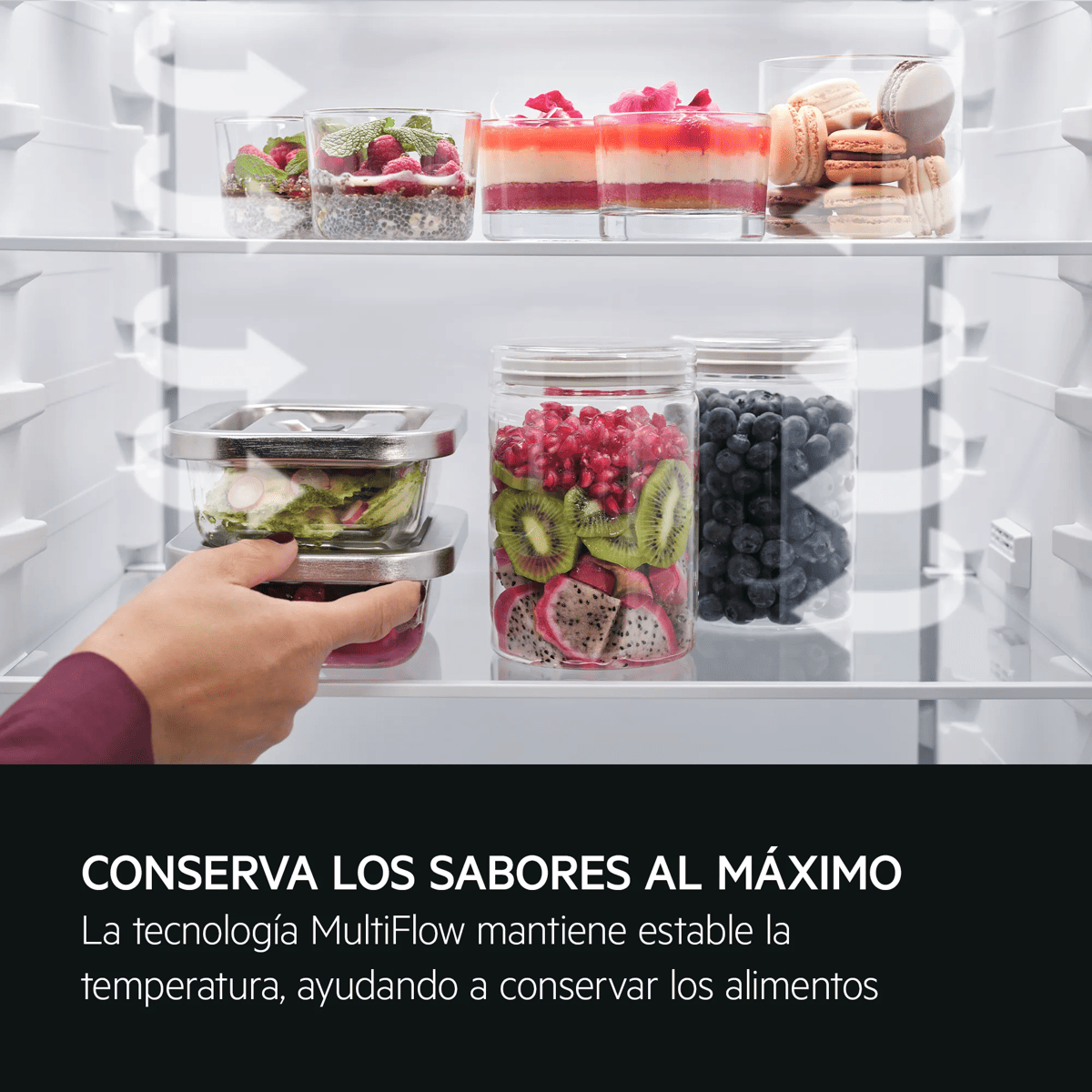 Una mano agarra recipientes con frutas y postres dentro de un refrigerador.