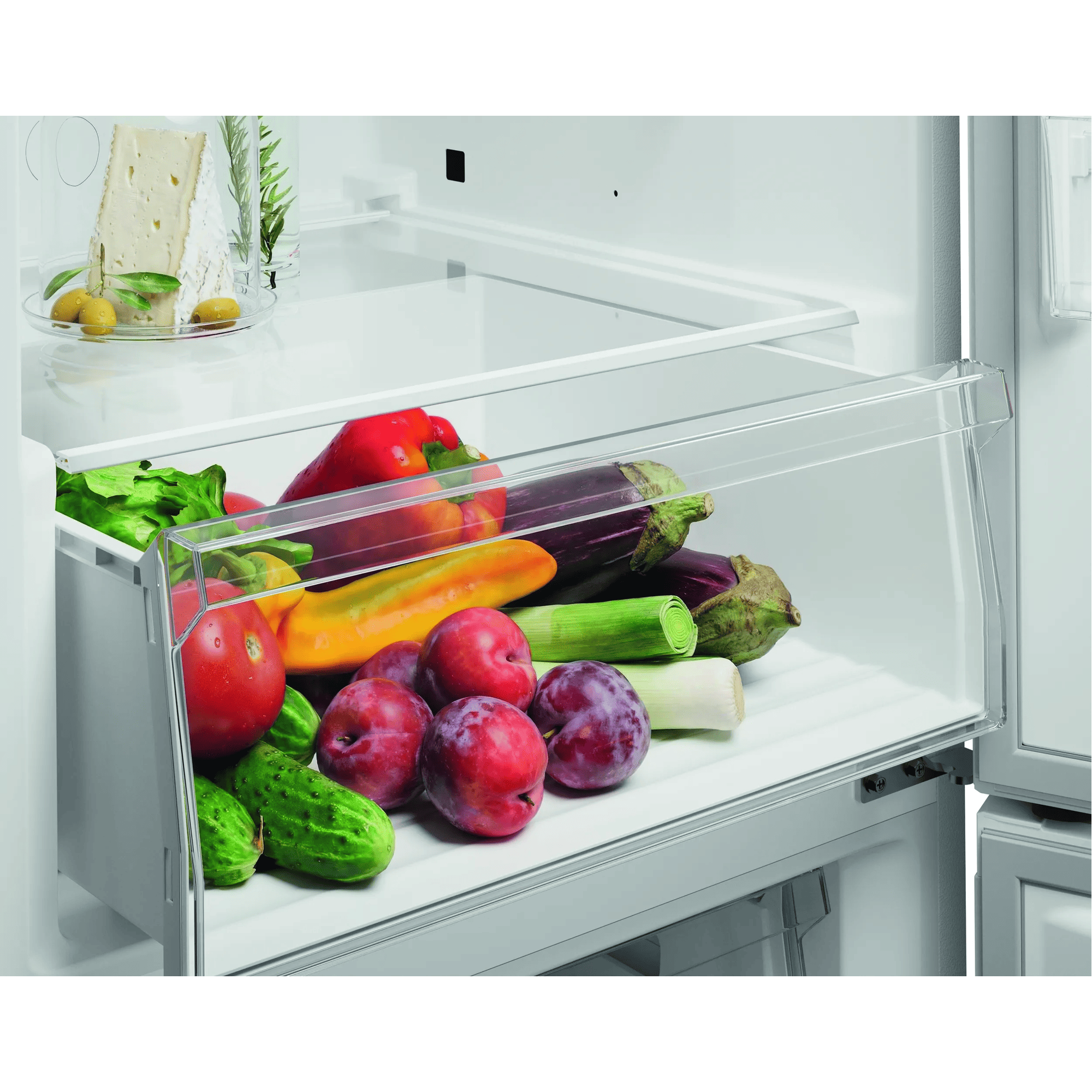 Un cajón de refrigerador lleno de verduras frescas como tomates, pepinos, pimientos, ciruelas y puerros.