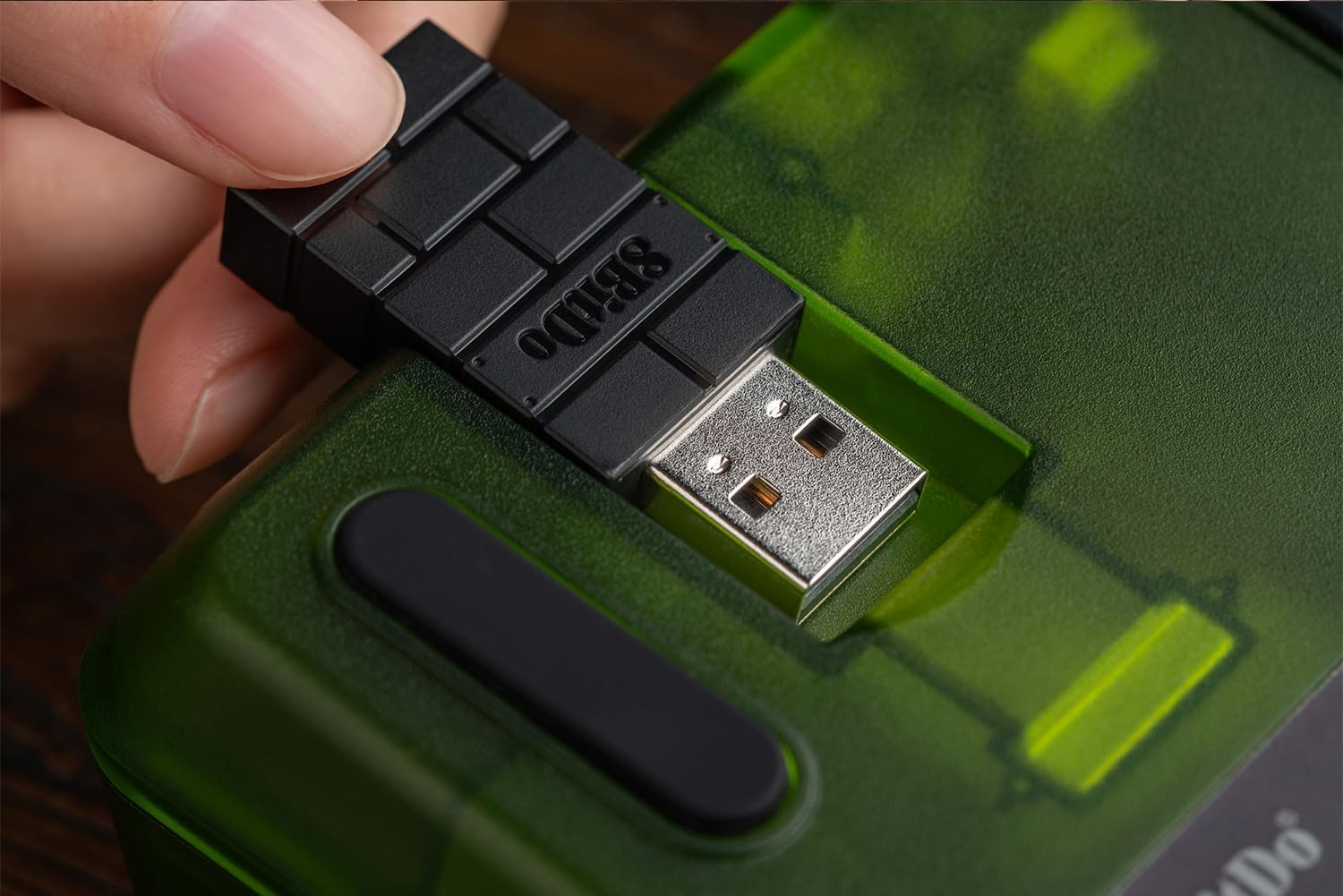 Palec wkłada czarny pendrive z napisem "SBIDO" do przezroczystego zielonego urządzenia.
