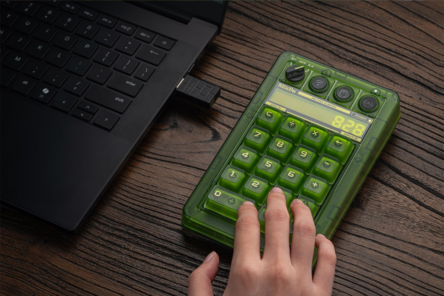 Dłoń używa zielonego kalkulatora numpad retro obok czarnego laptopa z podłączonym pendrivem USB.