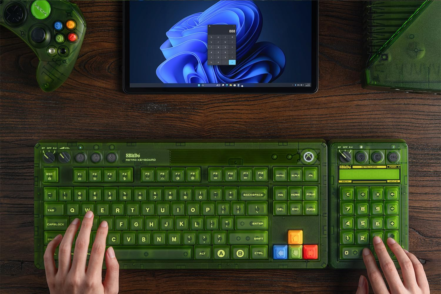 Zielony kontroler retro, klawiatura i tablet leżą na drewnianym stole.