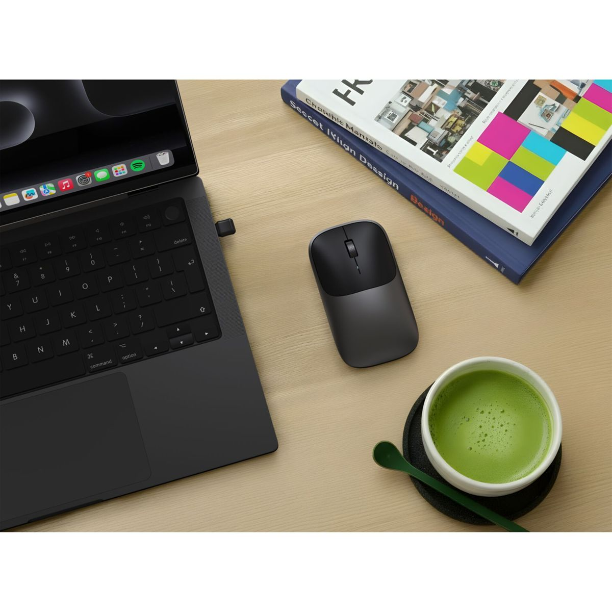 Een laptop, muis, boeken en een kop matcha thee op een houten bureau.
