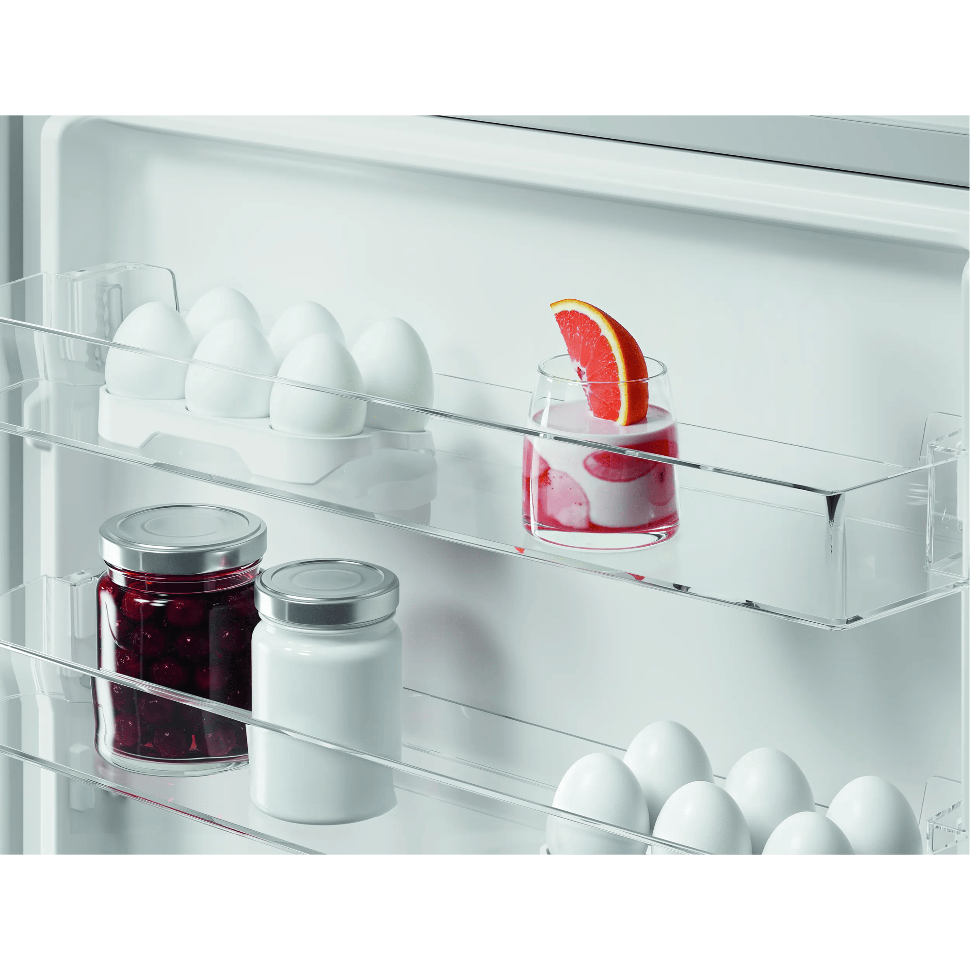 Huevos blancos en un estante de refrigerador, junto a un vaso de postre con pomelo.