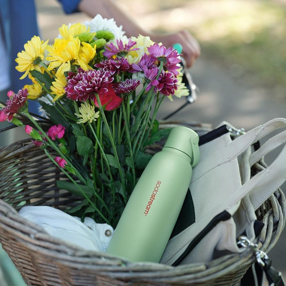 Ein Fahrradkorb mit Blumen und einer grünen Wasserflasche.