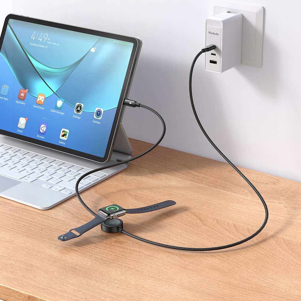 Ahşap bir masada tablet, akıllı saat ve şarj cihazı bulunuyor. Tablet şarja bağlı.