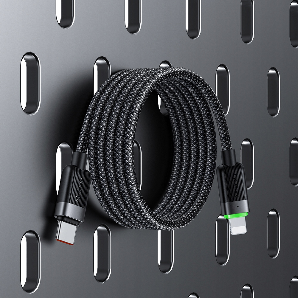 Sarmalanmış siyah örgülü USB-C - Lightning kablosu, koyu gri delikli panoda sergileniyor.