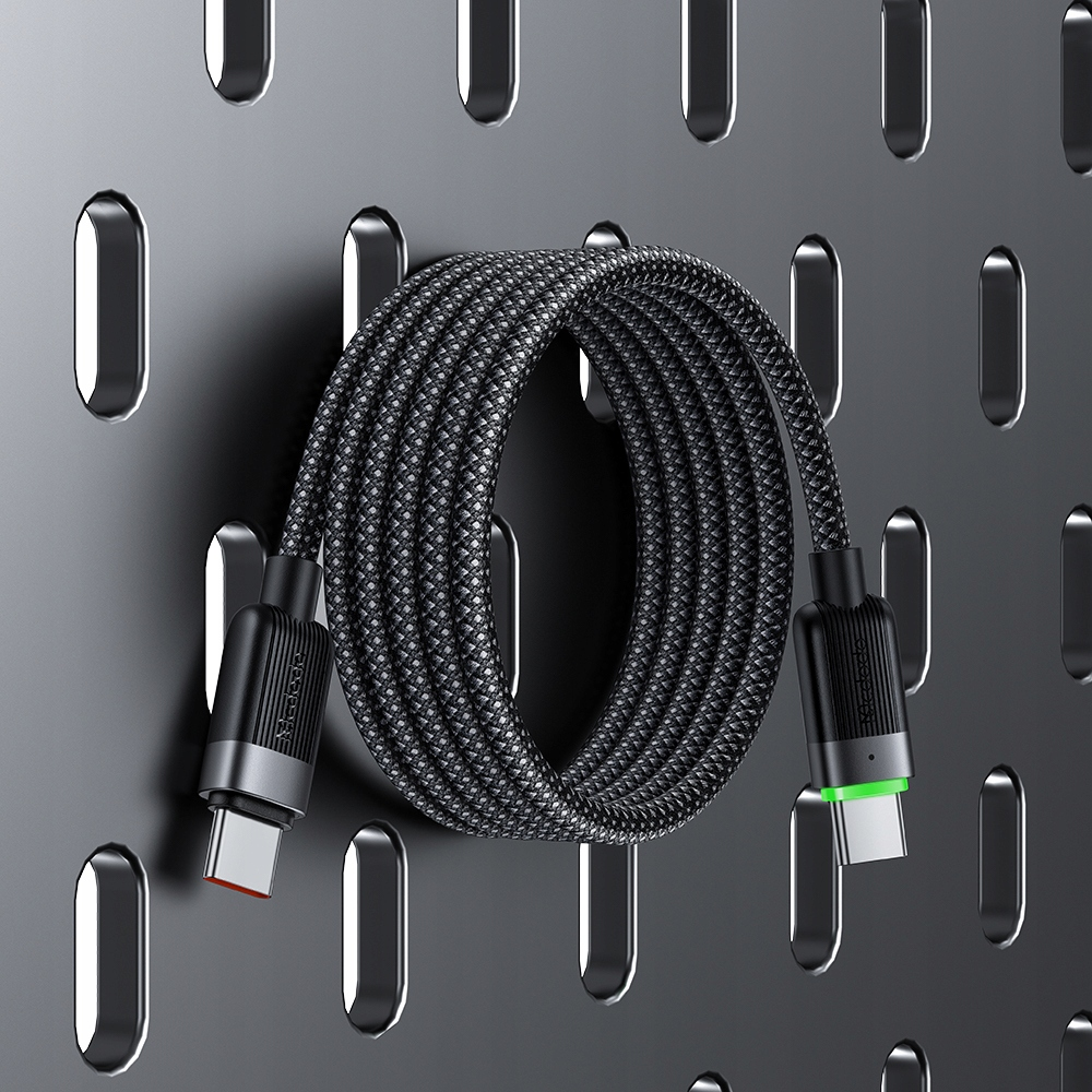 Gri örgüye sahip siyah USB-C kablo, delikli bir duvara sarılı.