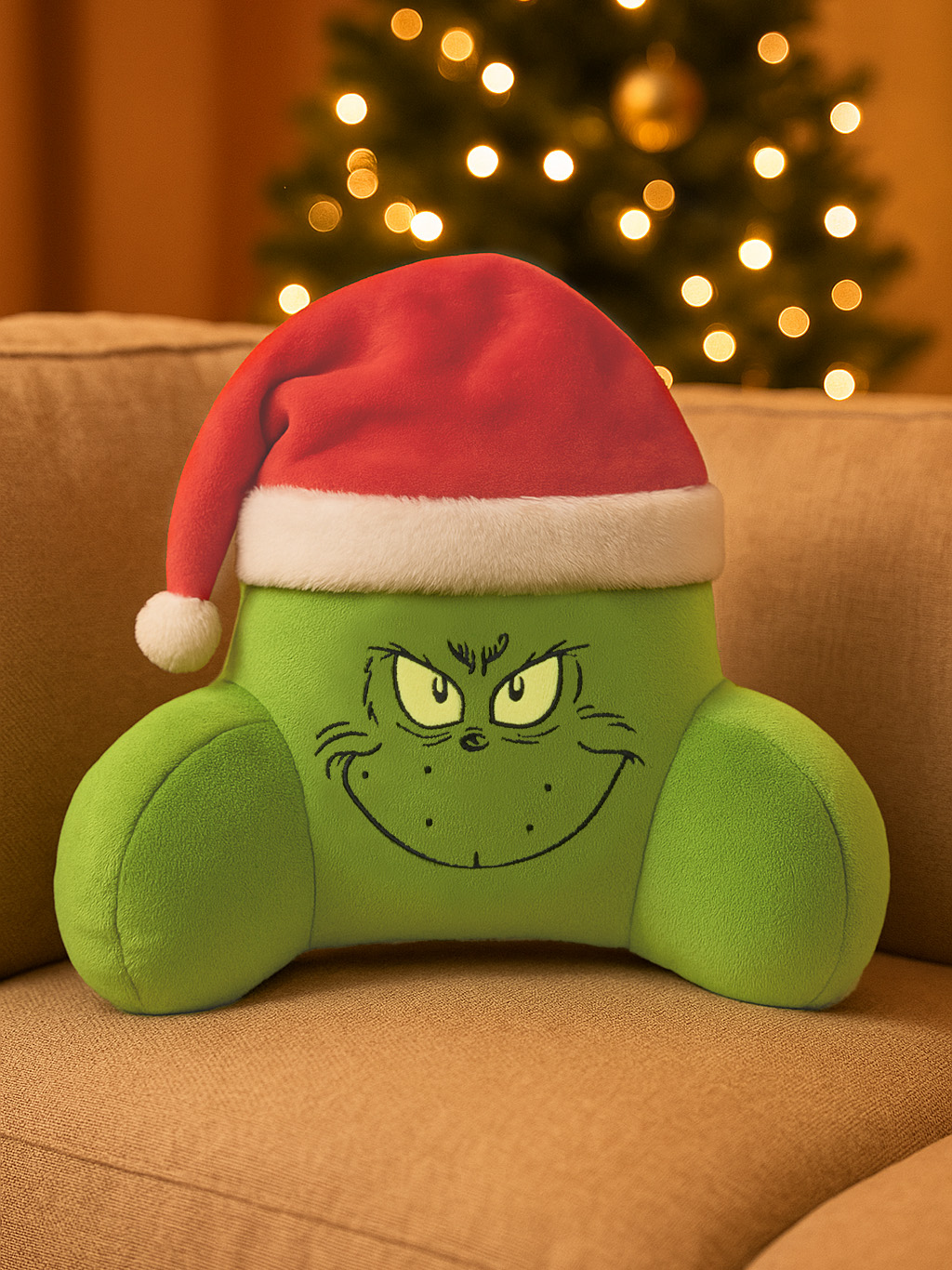 Grüner Grinch-Kissen mit Weihnachtsmütze auf Couch vor Weihnachtsbaum.