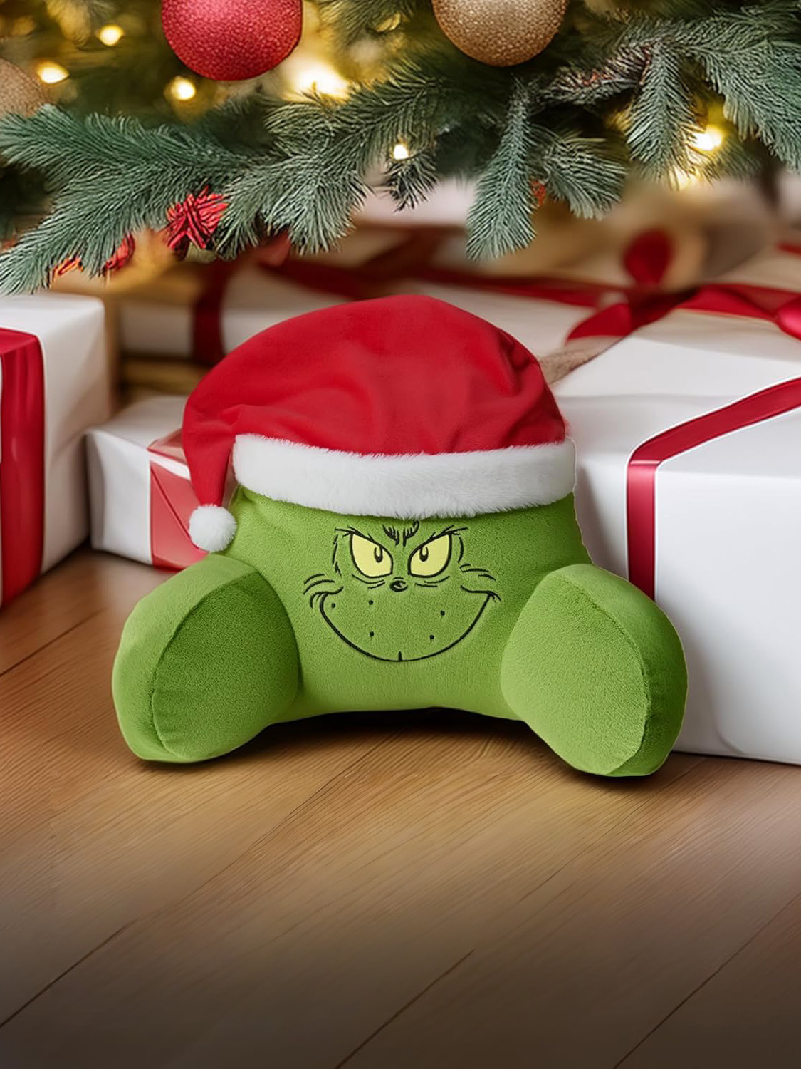 Grünes Grinch-Kissen mit Weihnachtsmütze unter einem Weihnachtsbaum mit Geschenken.