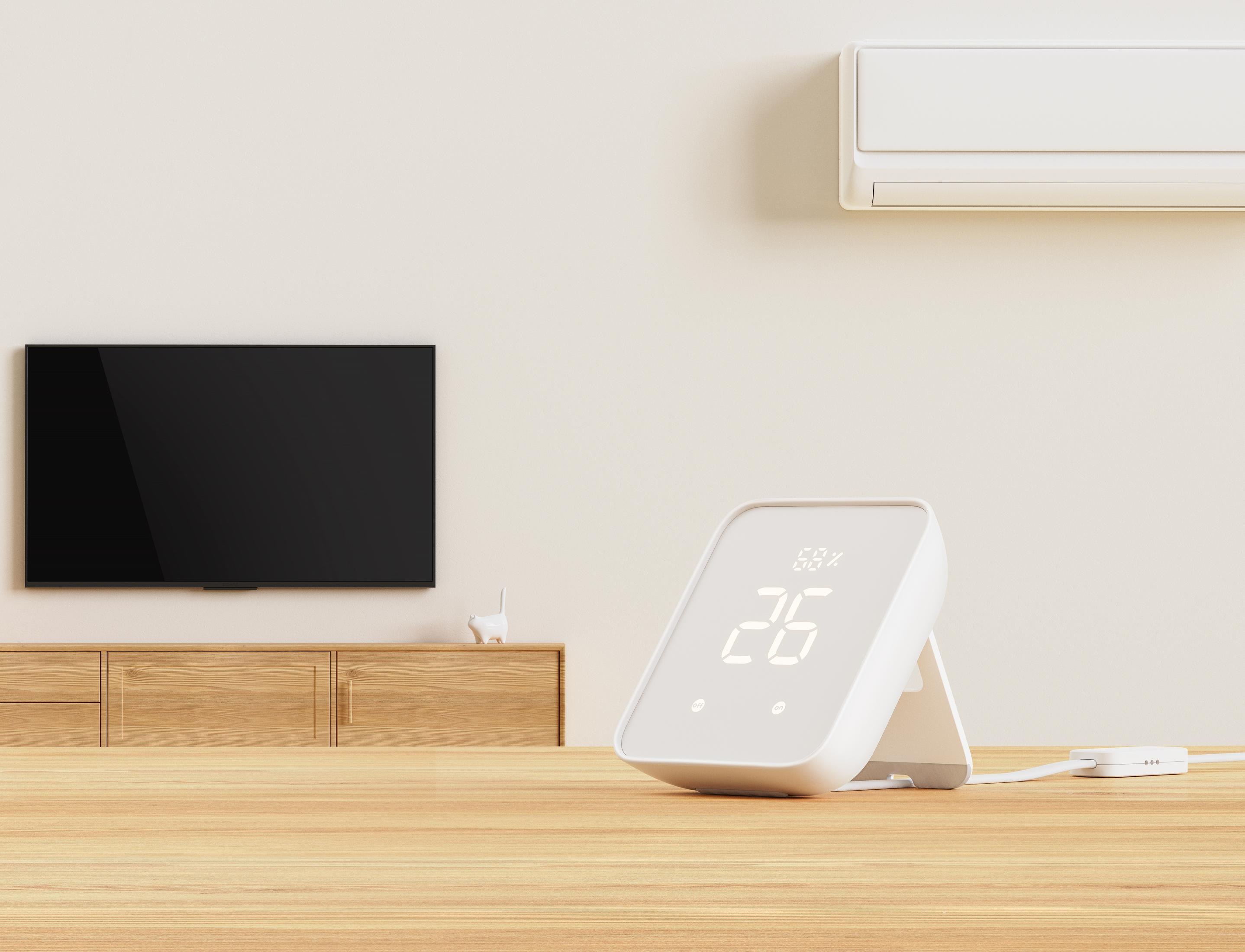 Ein weißes Klimagerät über einem Holzschrank mit Fernseher. Ein Thermostat steht vorne.