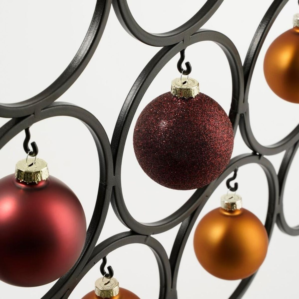 Drie kerstornamenten hangen aan een zwart metalen frame.