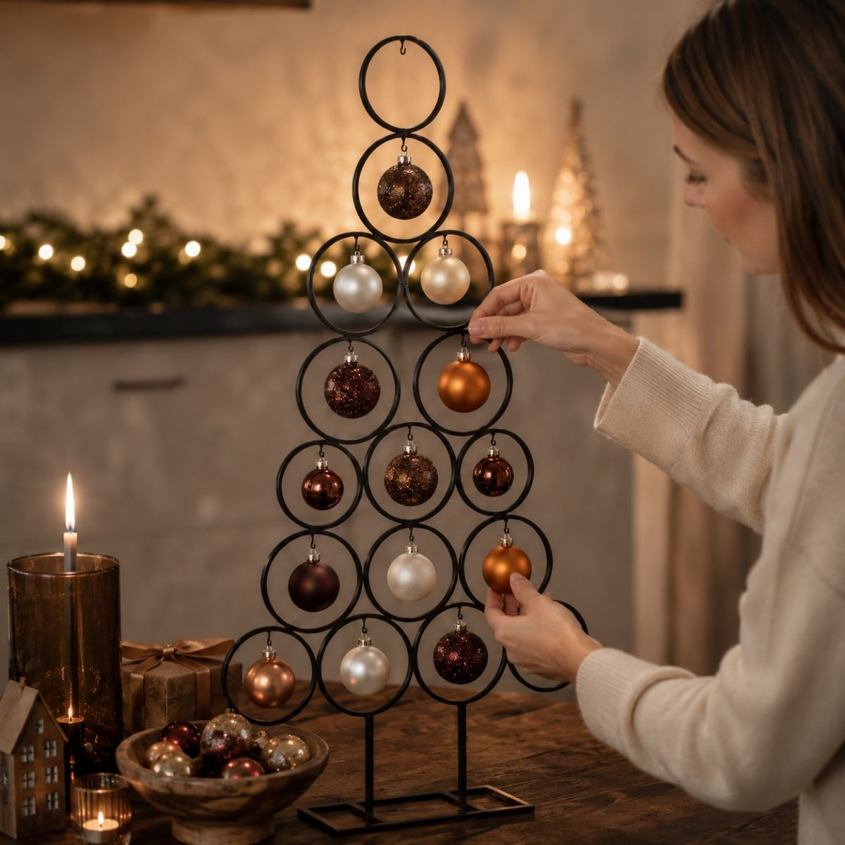 Vrouw versiert zwarte kerstboom met ornamenten. Kaarsen, cadeaus op voorgrond.