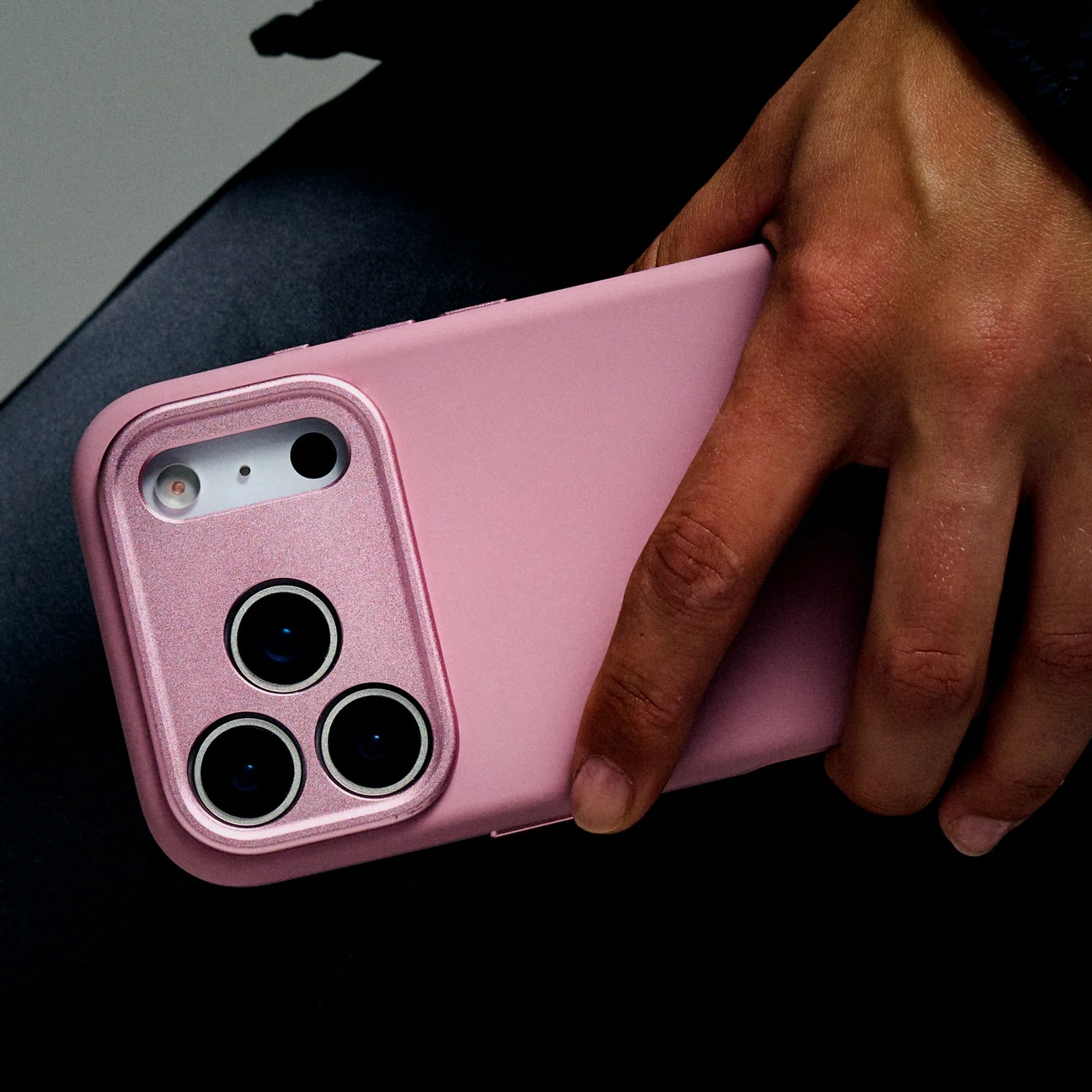 Una mano tiene un telefono rosa con tre fotocamere.
