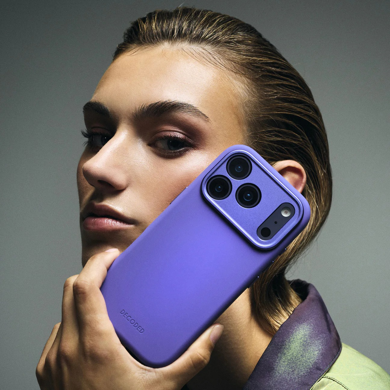 Eine Frau hält ein lila iPhone mit drei Kameras vor ihr Gesicht.