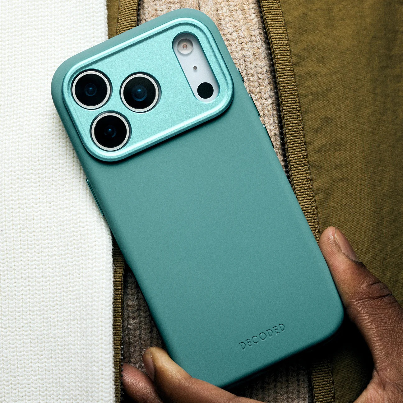 Una custodia per telefono verde acqua con tre fotocamere poggia su tessuti.