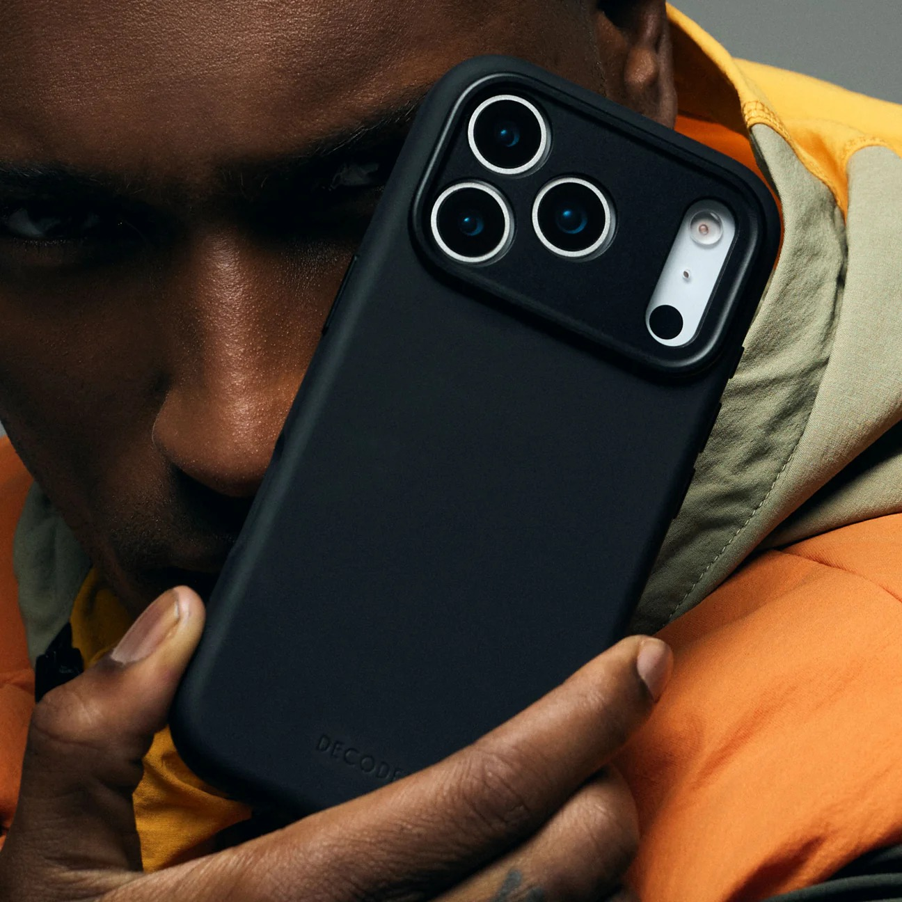 Ein Mann hält ein schwarzes iPhone-Case mit drei Kameras vor sein Gesicht.
