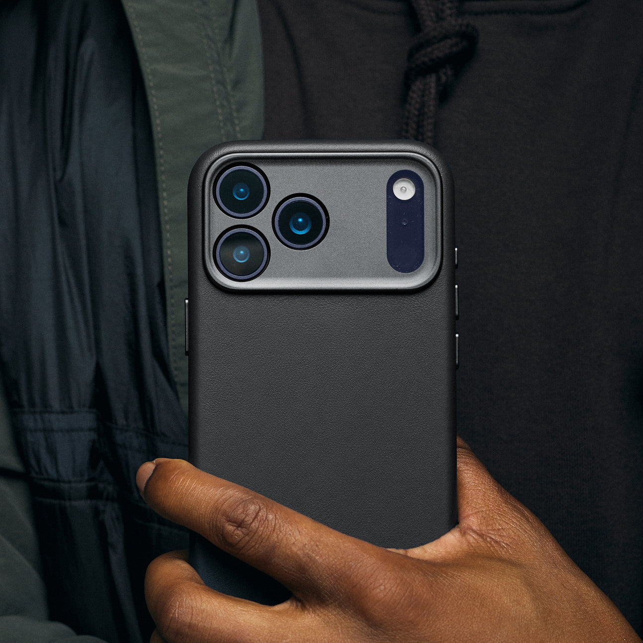Una persona tiene un telefono nero con fotocamera a triplo obiettivo. Un dito tocca il lato.