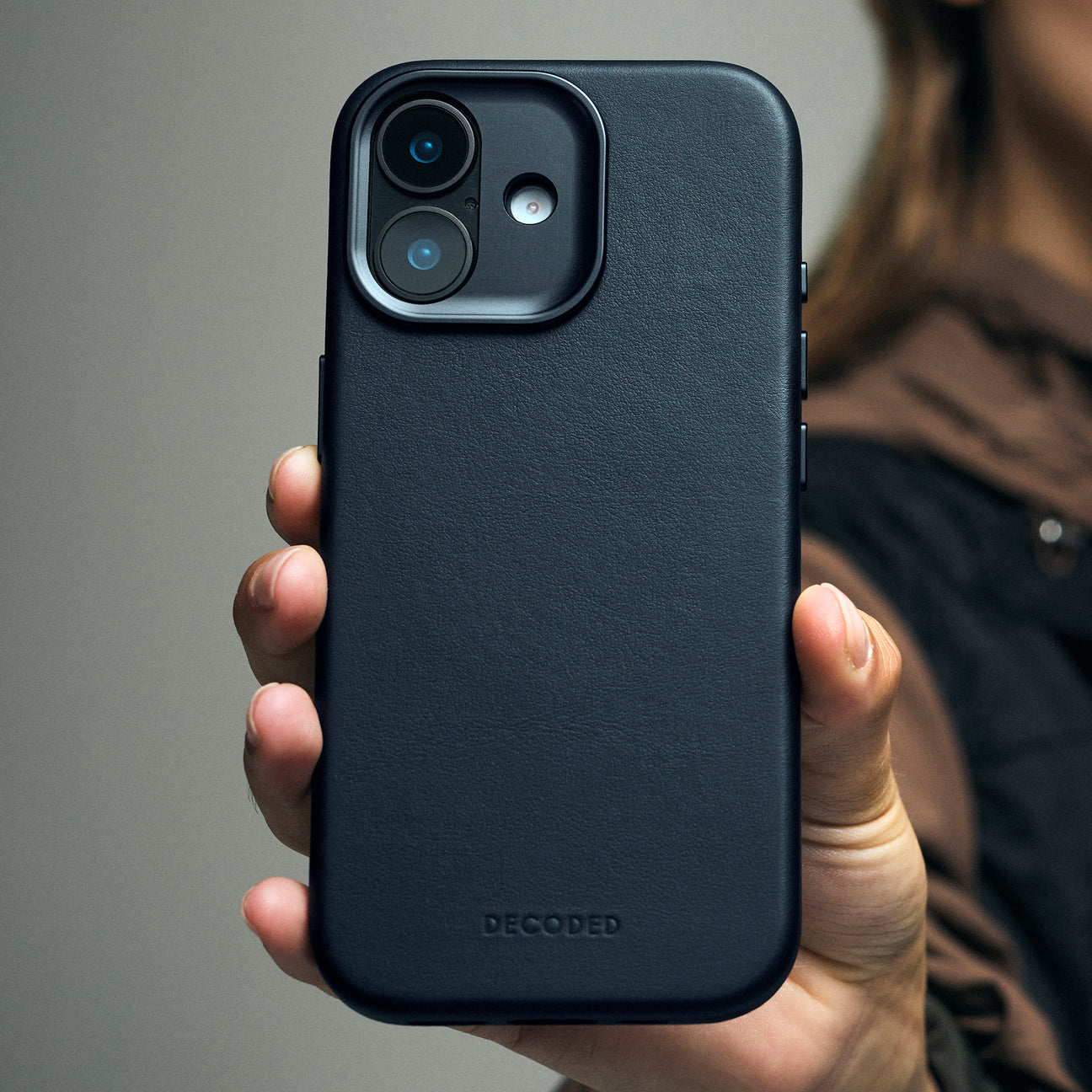 Una mano tiene una custodia scura e testurizzata per iPhone con fotocamera visibile.