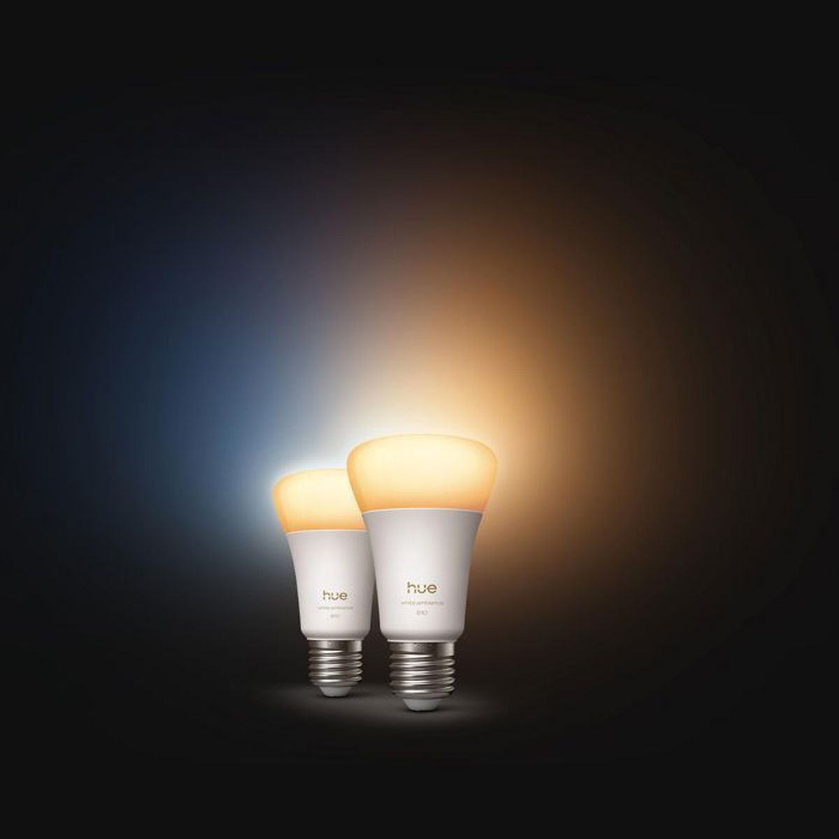 Due lampadine Hue bianche con base a vite brillano di luce calda e fredda su sfondo scuro.