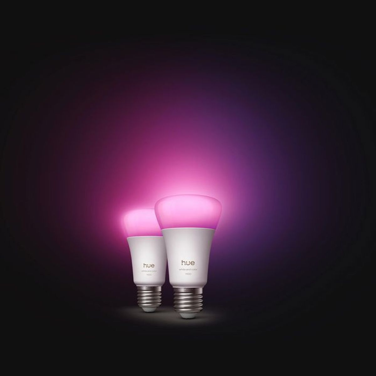 Due lampadine Philips Hue bianche brillano di rosa/viola su sfondo scuro.