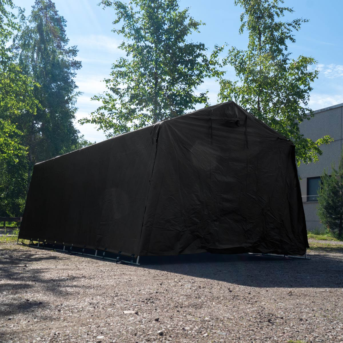 Ein schwarzes Zelt mit Metallrahmen steht auf einem Schottergrundstück unter Bäumen.