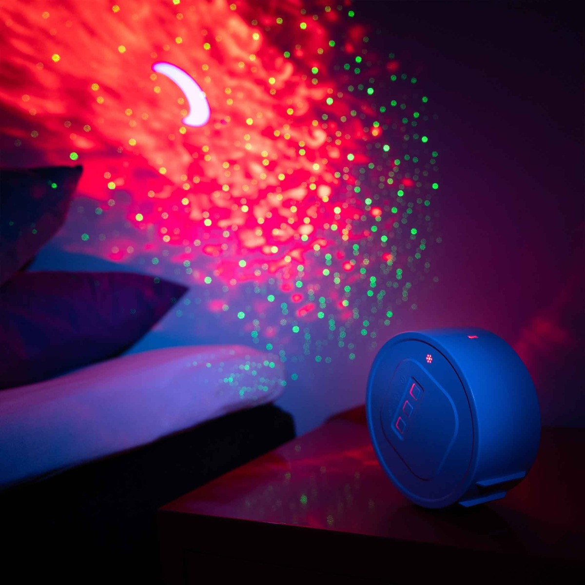 Ein blauer Projektor wirft rote und grüne Lichter und einen Halbmond an eine Wand über einem Bett.