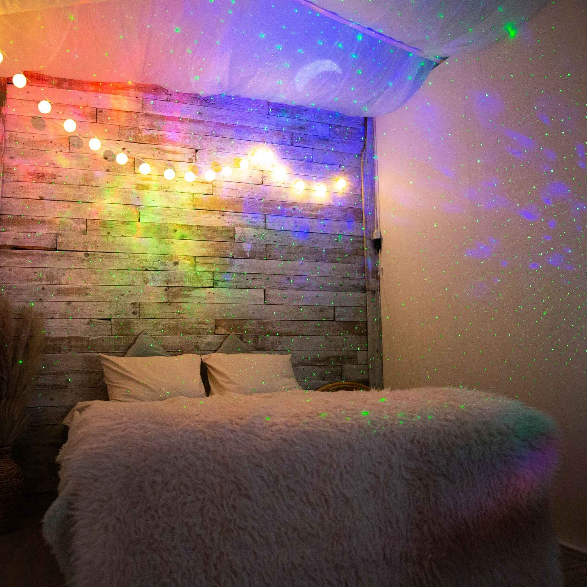 Ein Schlafzimmer mit Sternenprojektor, Lichterkette und Holzwand.