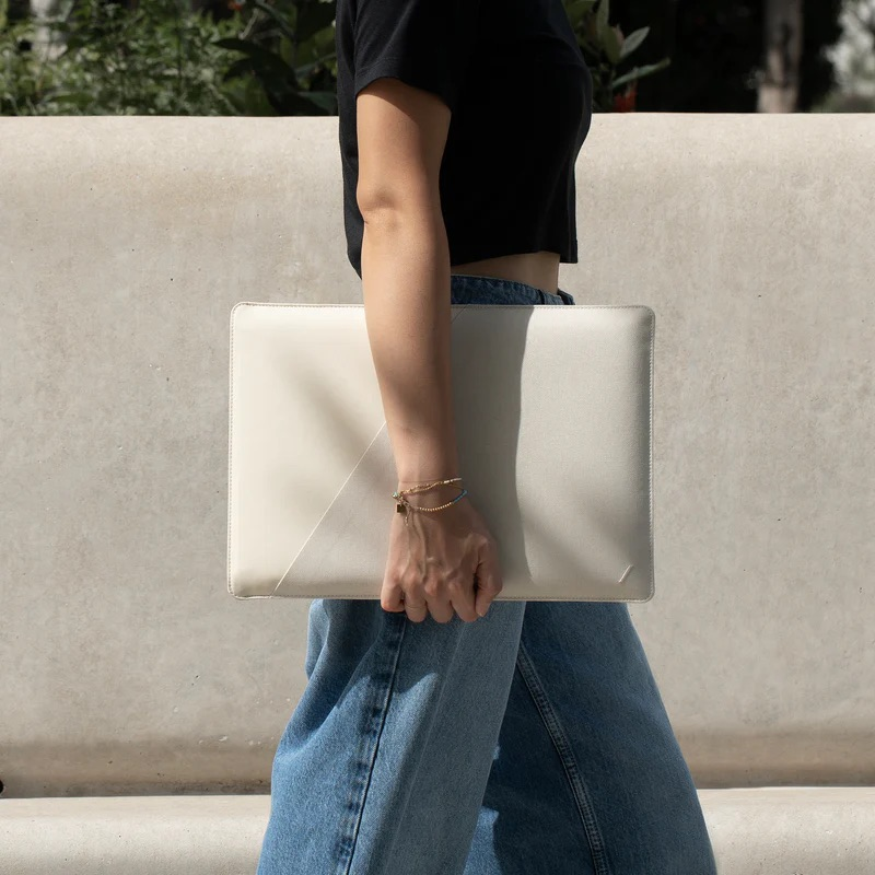 Una persona in jeans e top nero porta una borsa per laptop bianca.