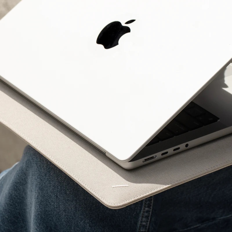 Un laptop bianco con logo Apple poggia su jeans e custodia grigio chiaro.