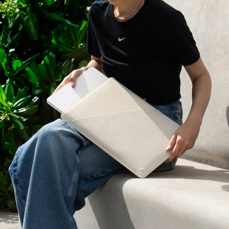 Una persona in jeans e maglietta nera tiene una custodia per laptop beige.