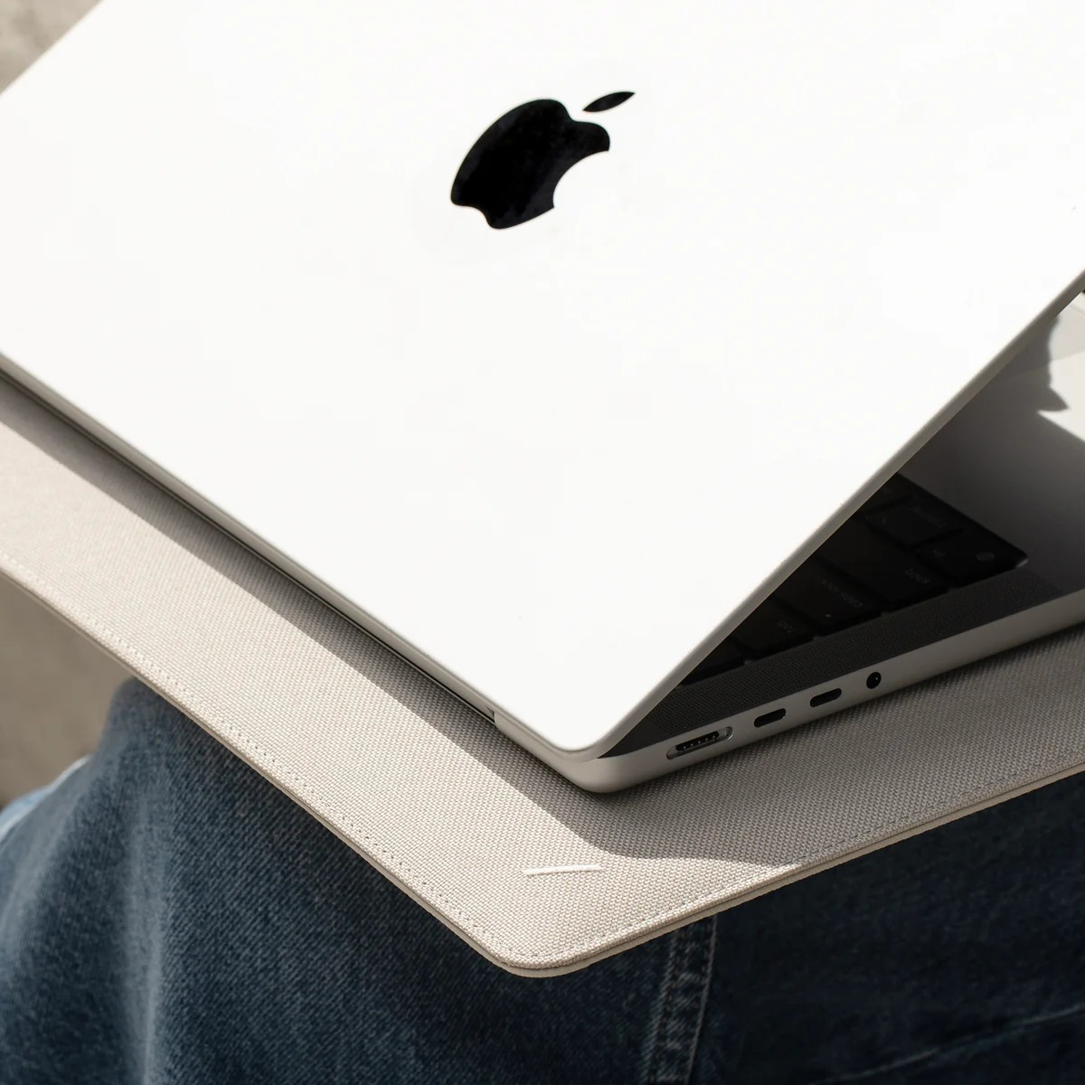 Un laptop bianco con logo Apple poggia su tessuto grigio e jeans blu.
