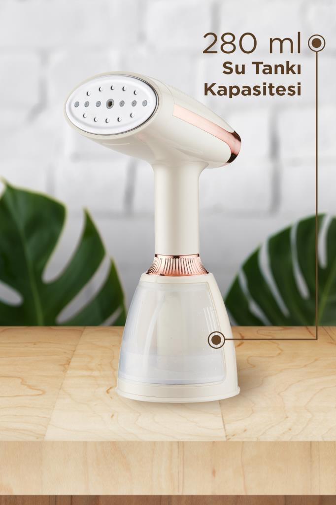 Ahşap masa üzerinde, arkasında yeşil yapraklar olan, rose gold detaylı beyaz buharlı ütü.