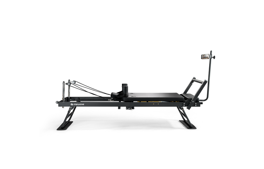 Un reformer de Pilates negro con poleas, correas y un poste con soporte para teléfono.