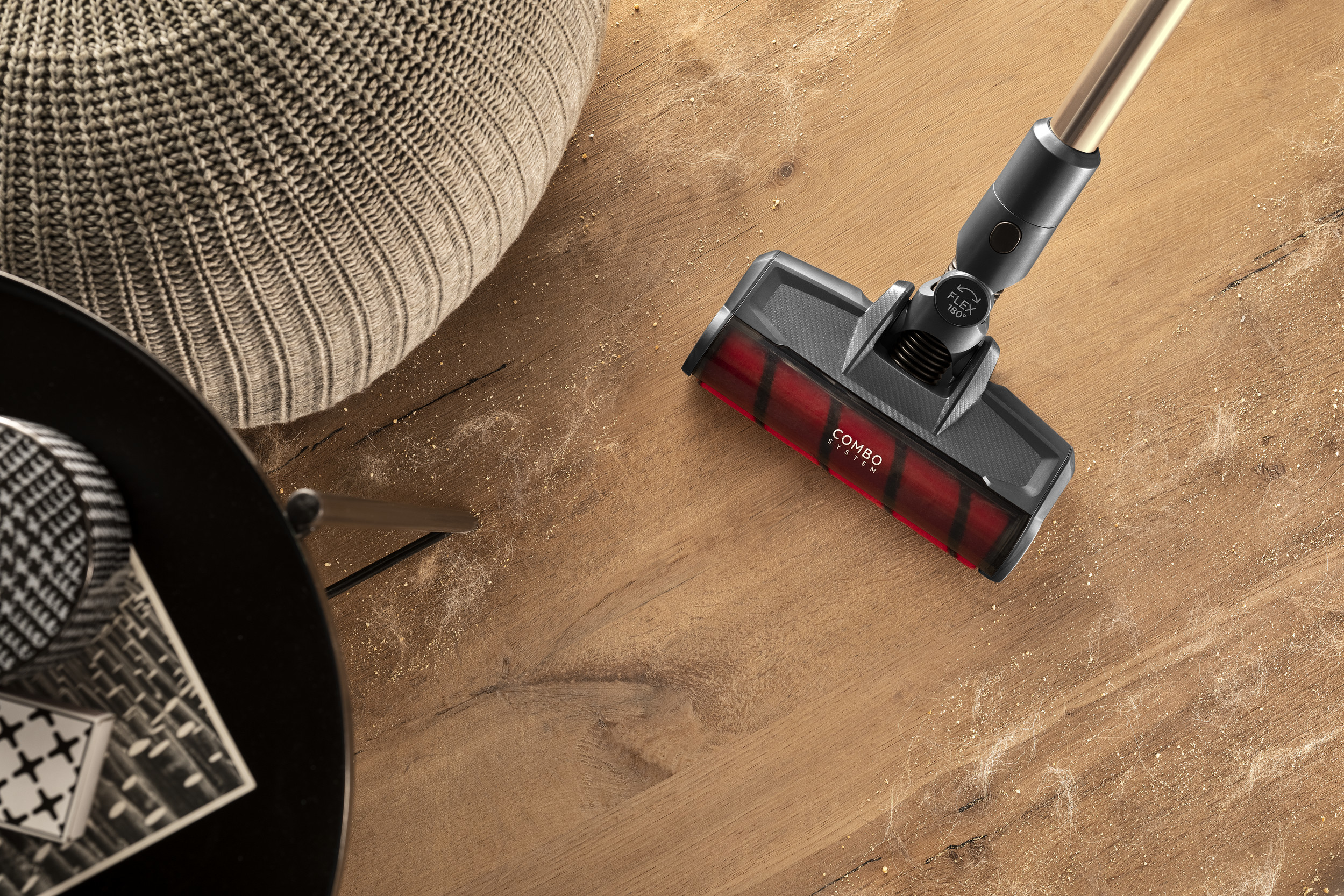 Testina aspirapolvere con spazzola rossa su pavimento in legno con polvere.