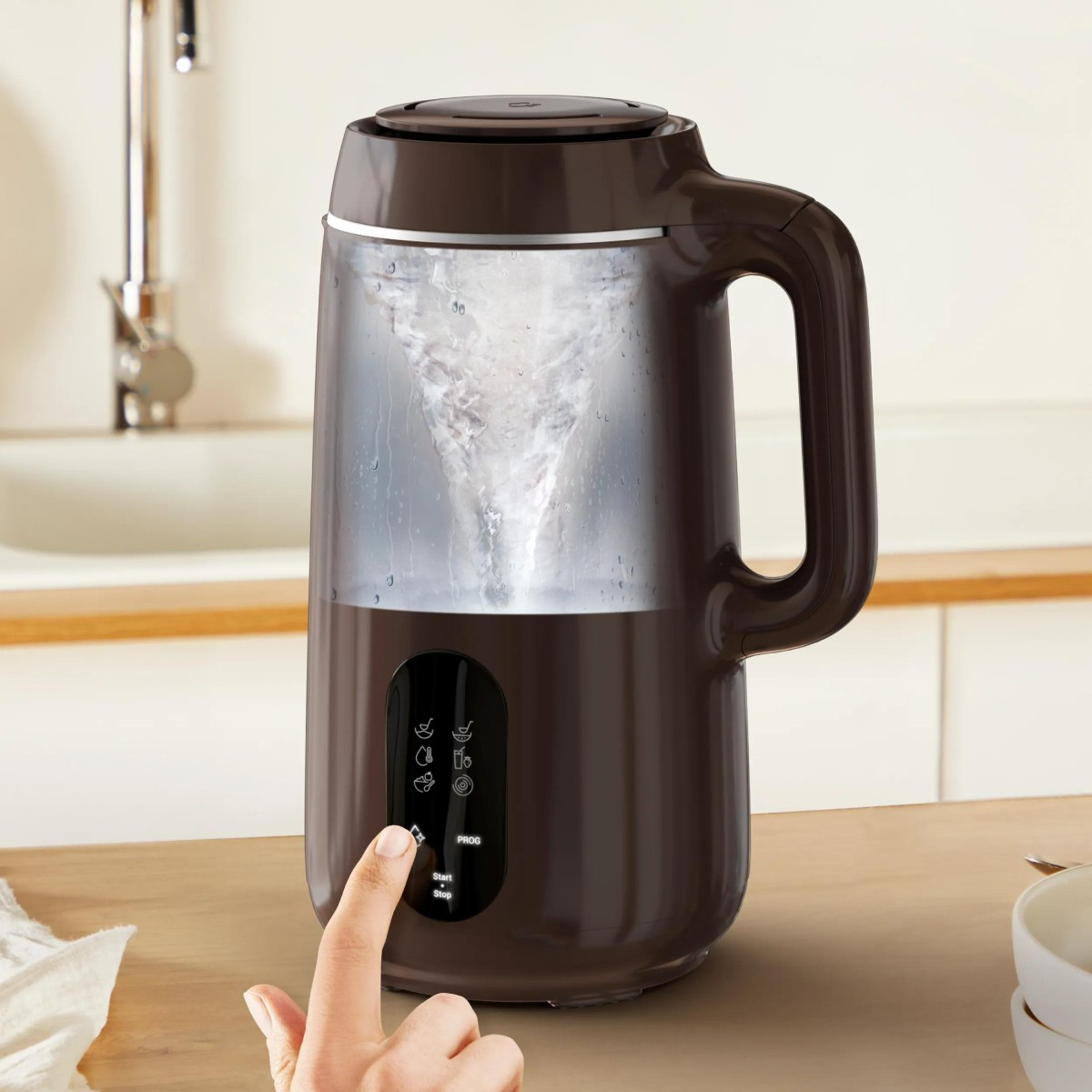 Un elettrodomestico da cucina marrone con un vortice d'acqua all'interno. Una mano preme un pulsante.