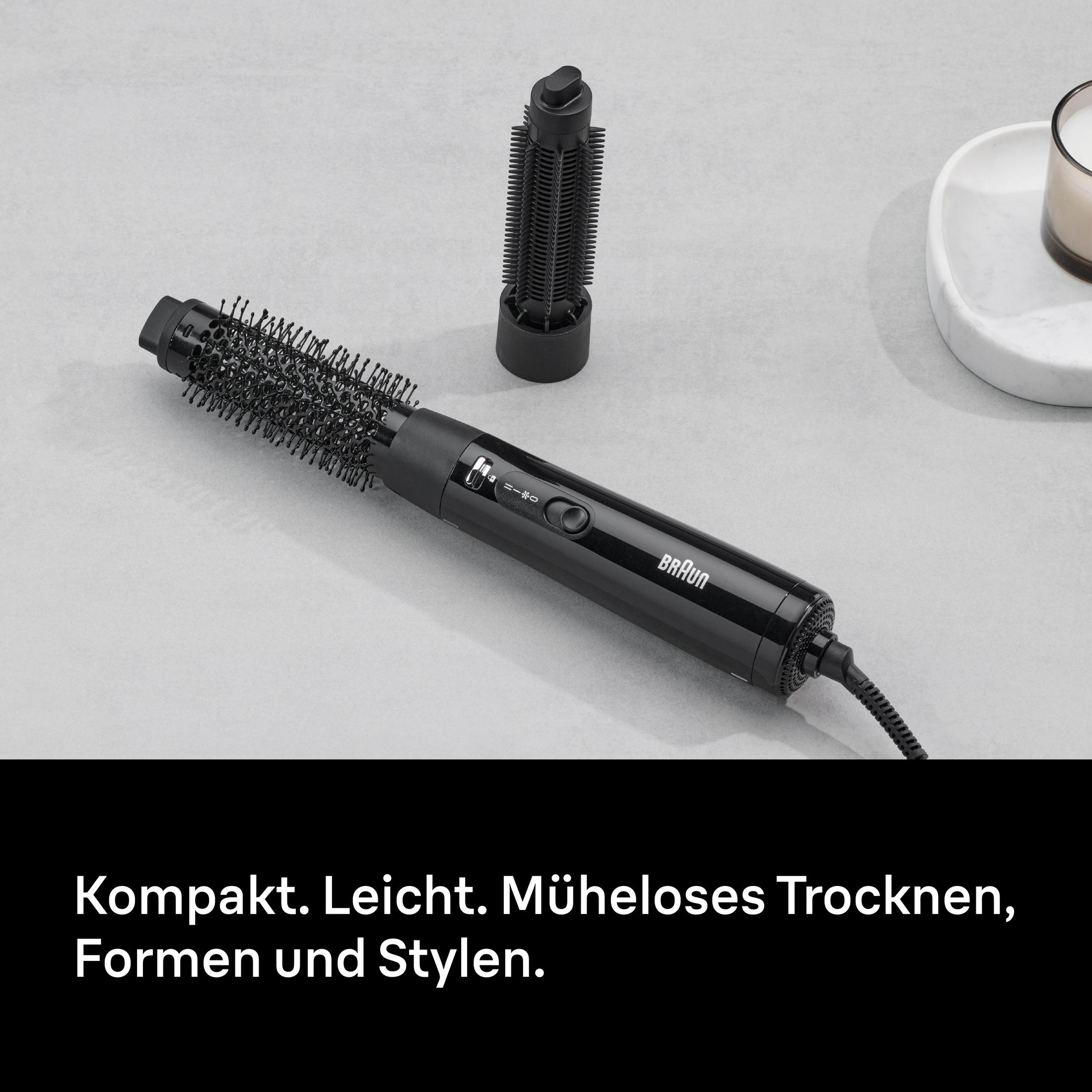 Ein schwarzer Braun-Haartrockner mit Aufsätzen auf grauem Hintergrund.