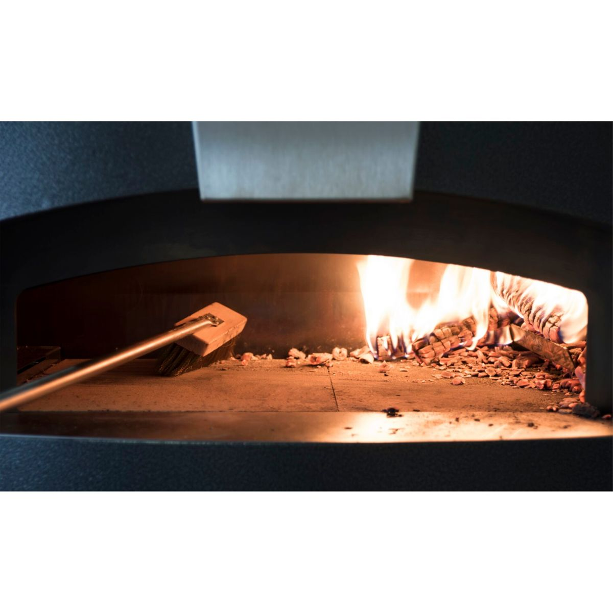 Ein Besen reinigt den Boden eines Pizzaofens, während Holz darin brennt.