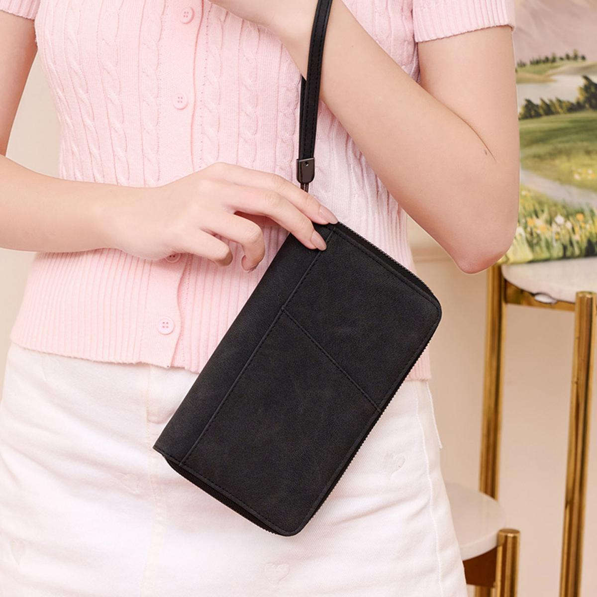 Eine Person hält eine schwarze Brieftasche in der Hand, die sie vor sich trägt.