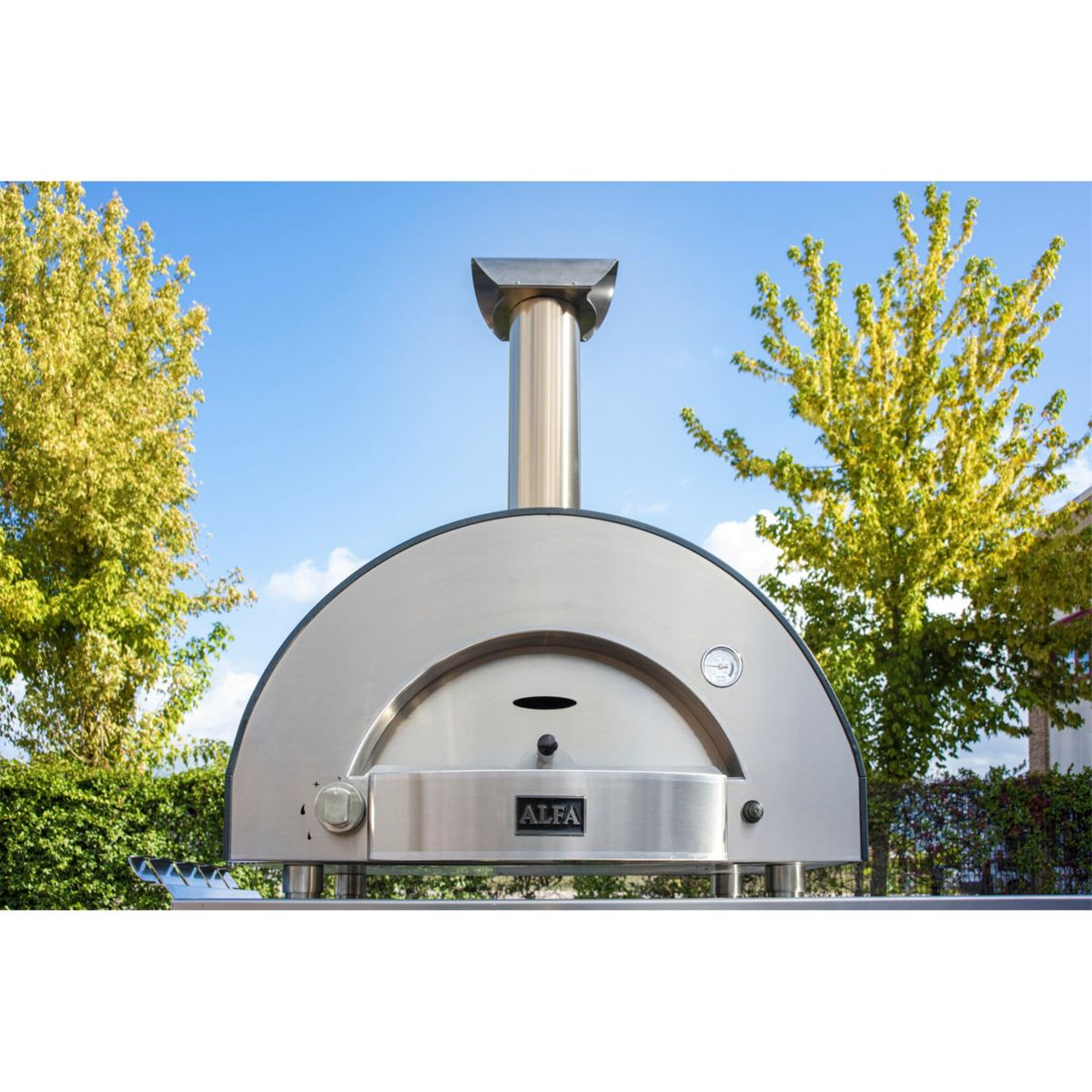 Ein silberner Pizzaofen mit Schornstein steht draußen unter blauem Himmel.