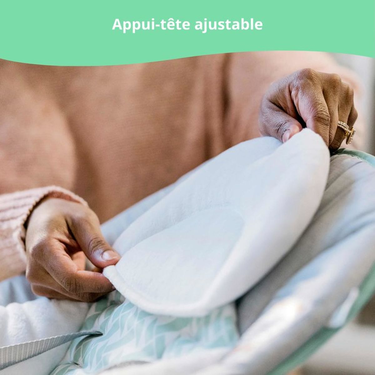 Eine Hand passt ein weißes Kopfpolster in eine Babywippe mit mintgrünem Muster ein.