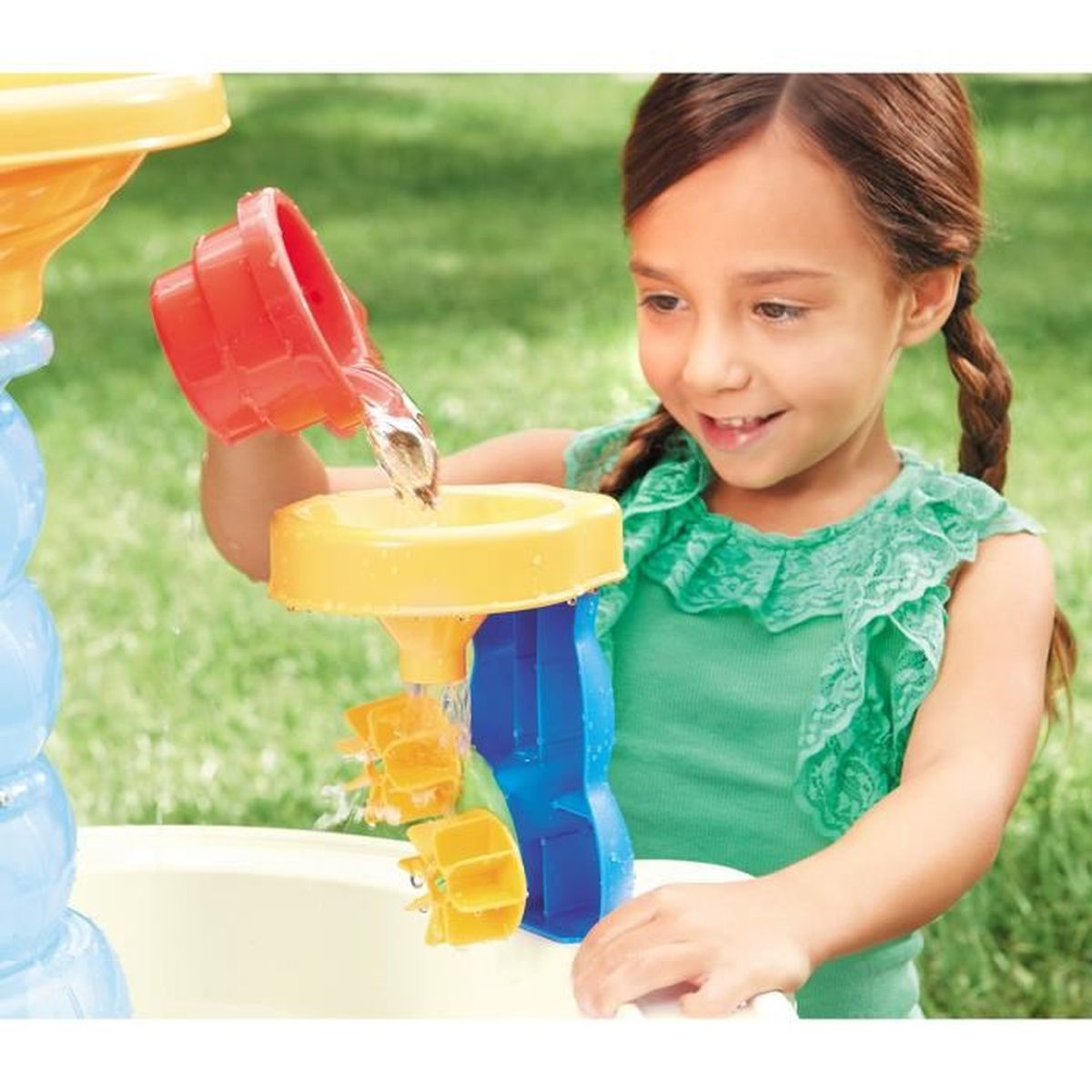 Una bambina versa acqua da una tazza rossa in un giocattolo giallo con ruote idrauliche.