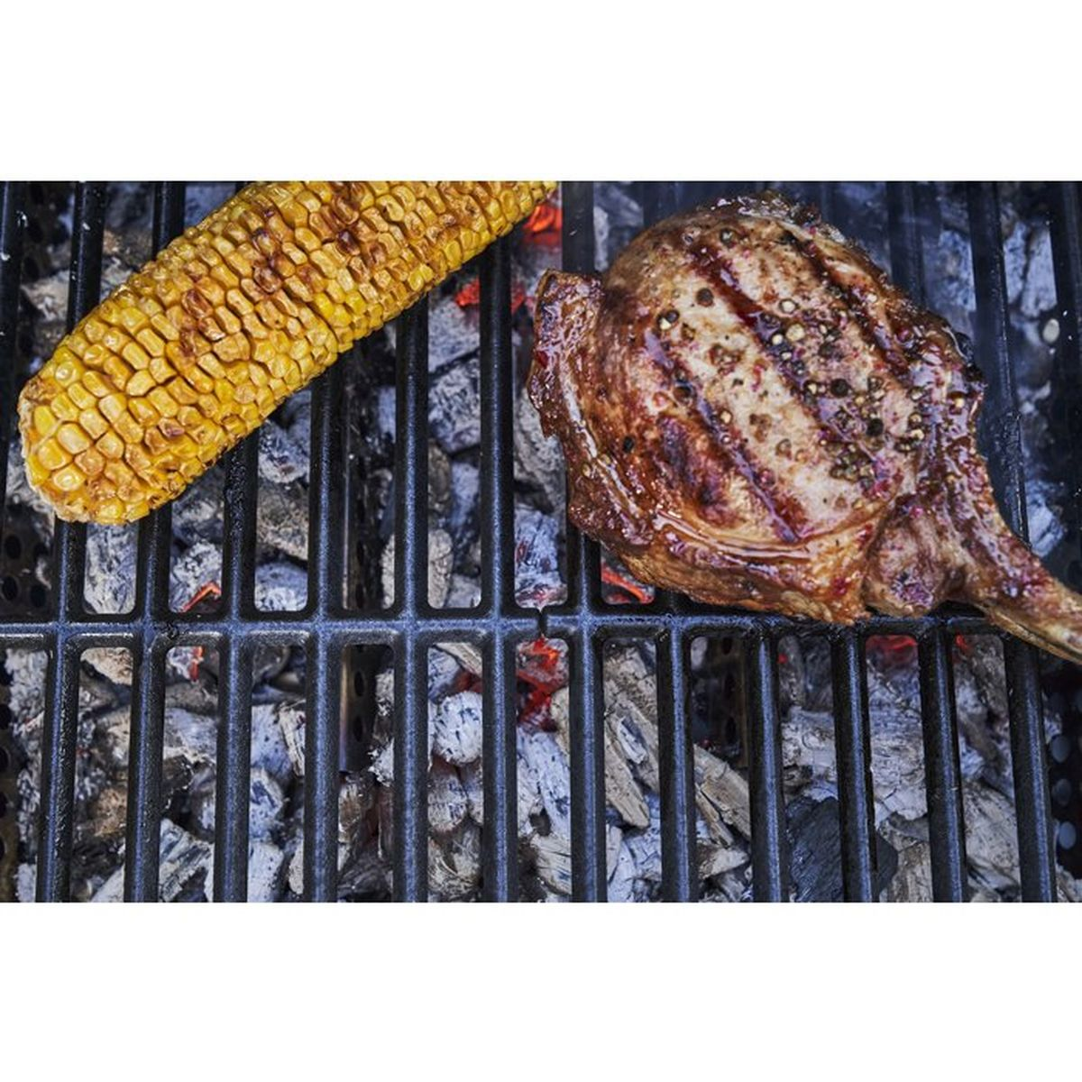 Una bistecca alla griglia e pannocchie di mais riposano su una griglia su carboni ardenti.
