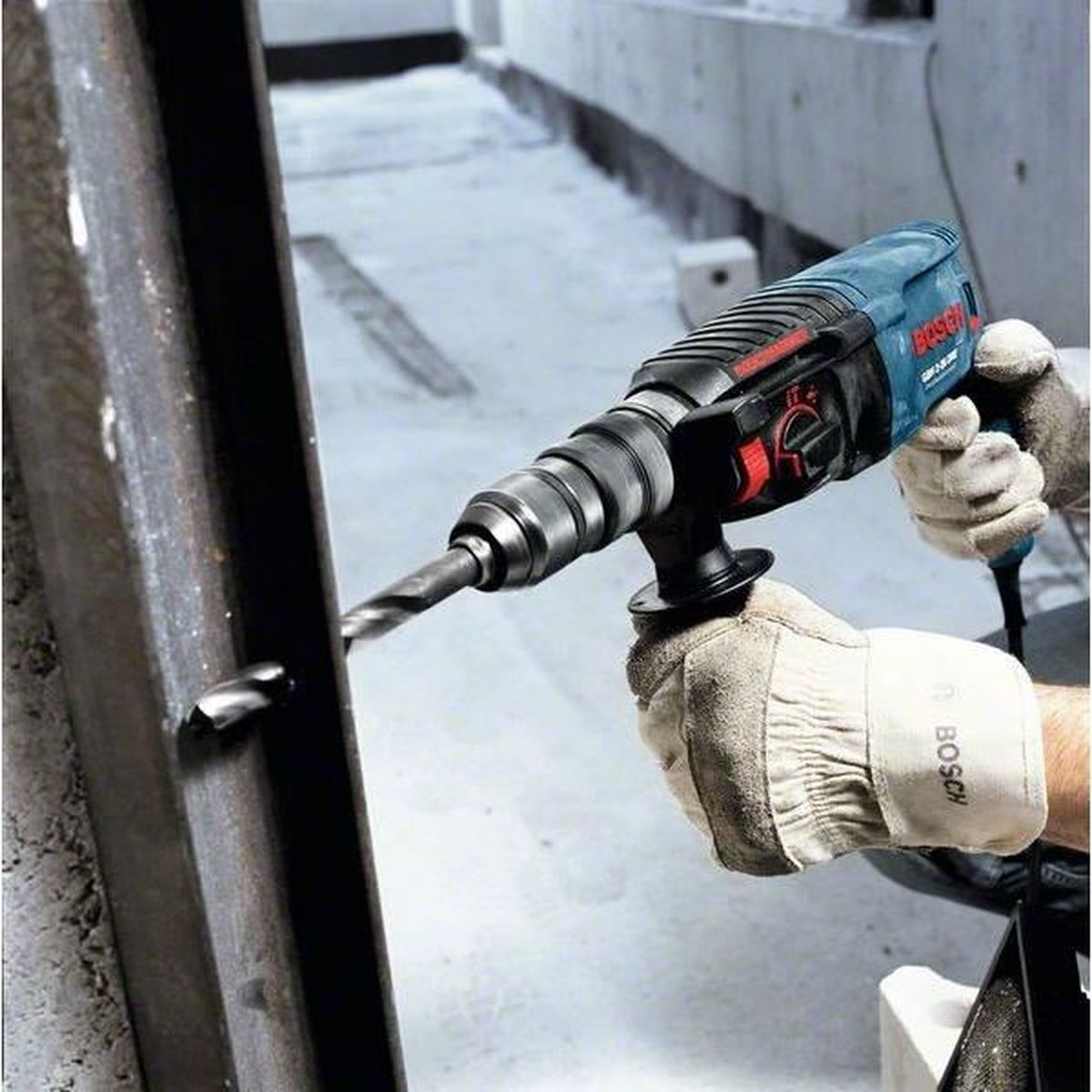 A man drills into a metal pipe with a blue Bosch hammer drill.