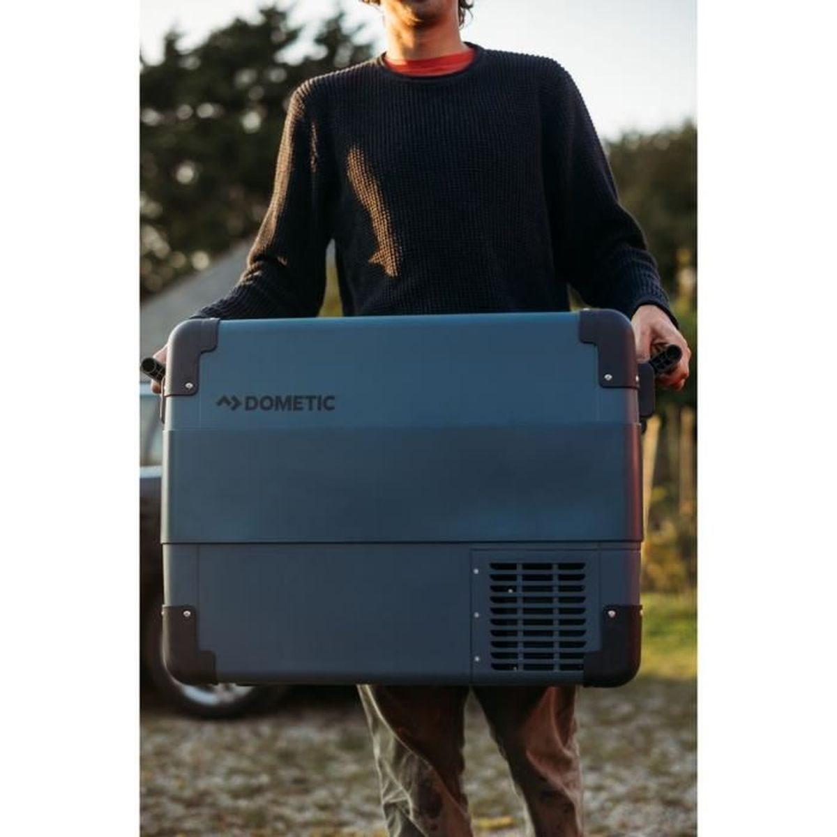 Een man draagt een donkerblauwe Dometic koelbox buiten.