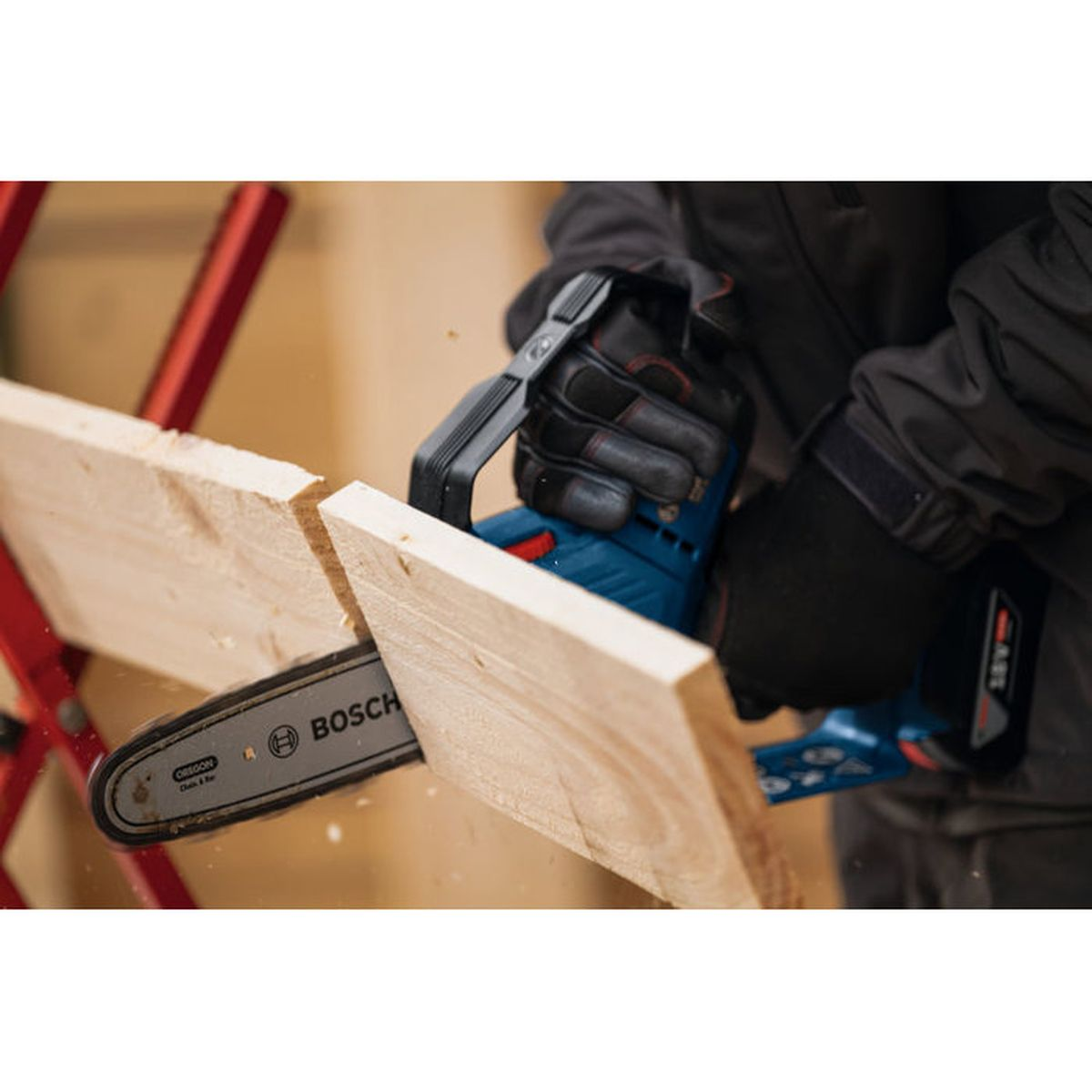 Person mit Handschuhen schneidet Holz mit einer blauen Kettensäge.