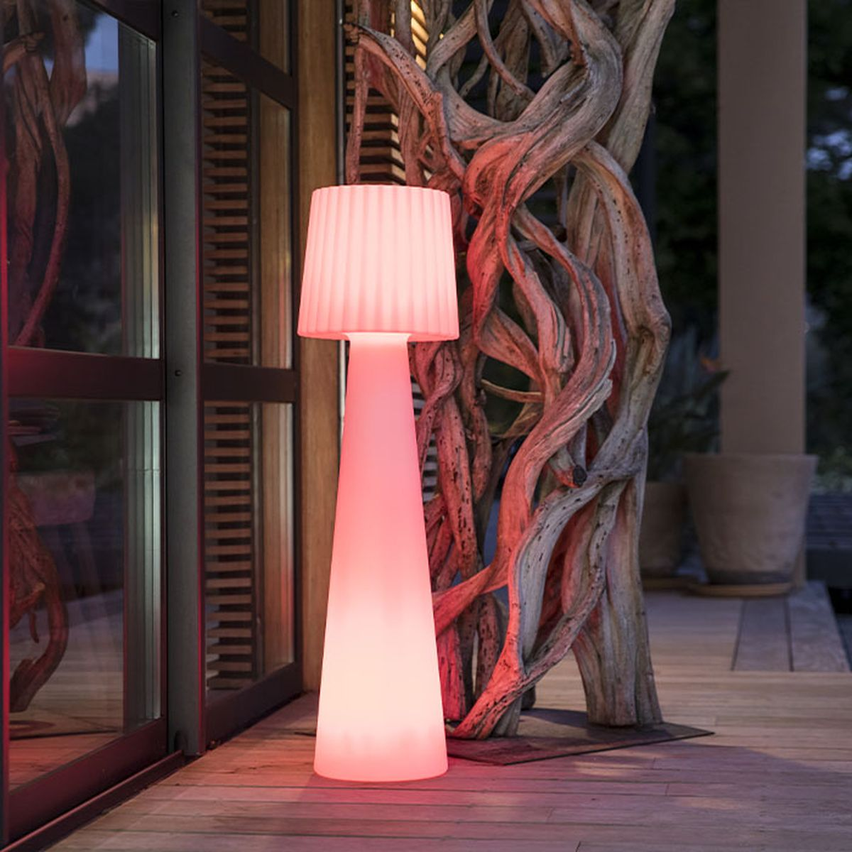 Una lampada da terra illuminata di rosso brilla accanto a un tronco d'albero nodoso su un ponte di legno.