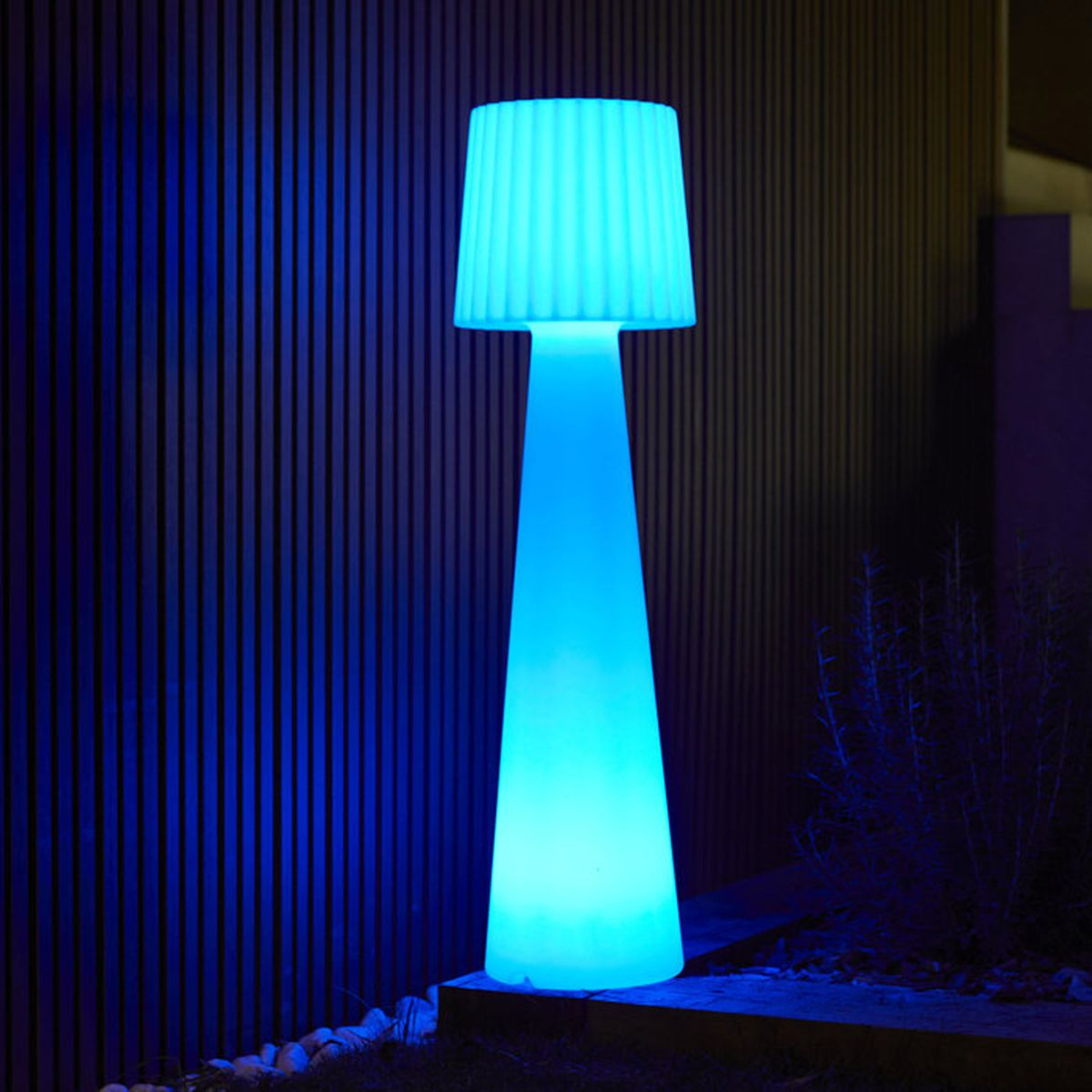 Una lampada da terra blu luminosa con paralume a coste si trova all'aperto.