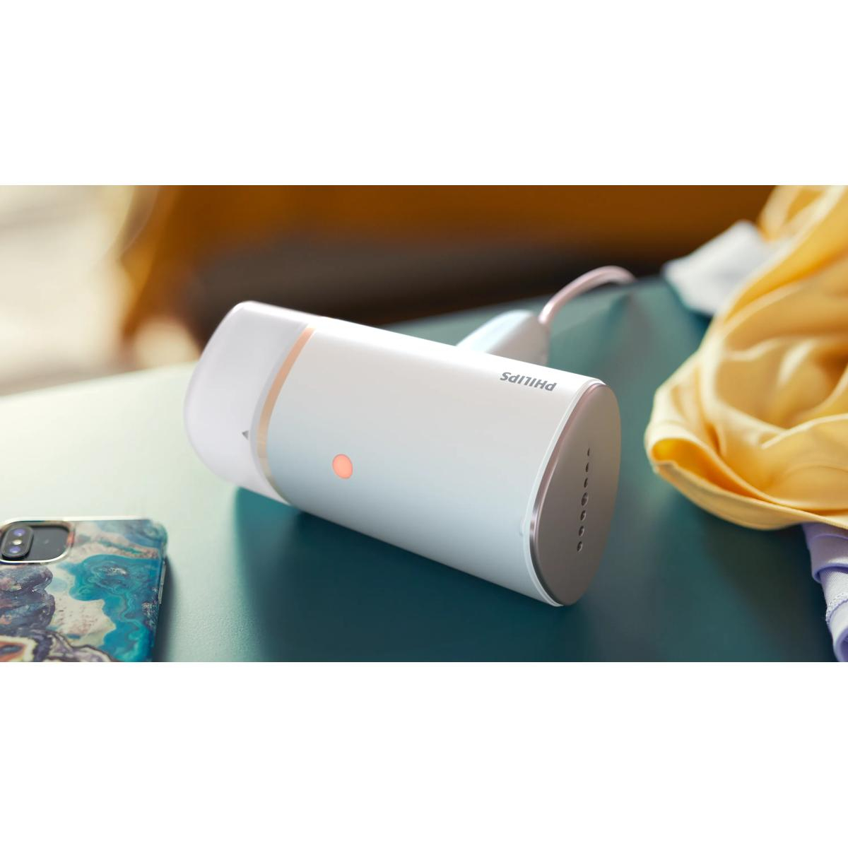 Turkuaz yüzeyde turuncu ışıklı beyaz Philips el ütüsü duruyor. Yanında renkli kılıflı bir telefon var.